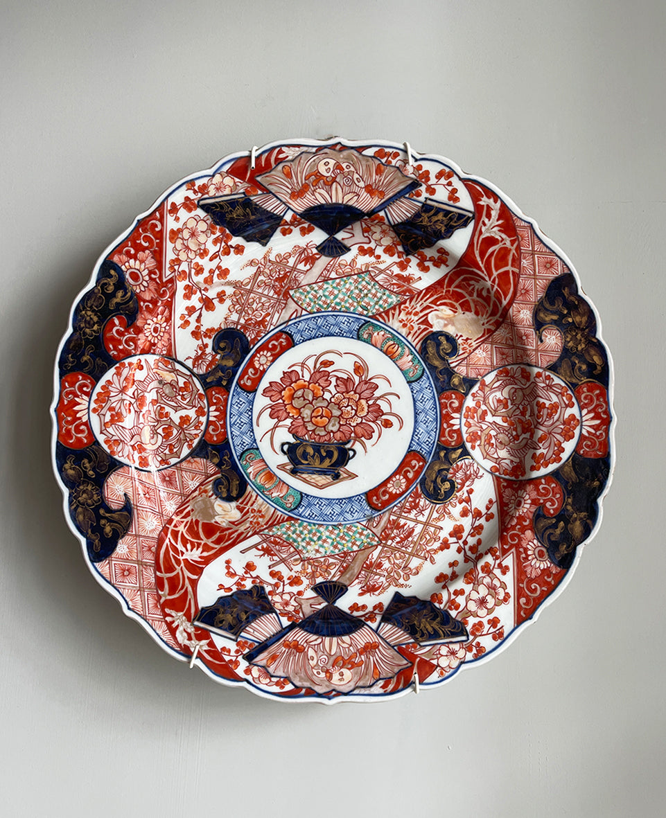 A large Oriental Imari scolloped edged plate with colourful hand painted depictions of Chrysanthemum flowers, fans, birds and cherry blossom. The underside sees a freeze of blue lilies - SHOP NOW - www.intovintage.co.uk