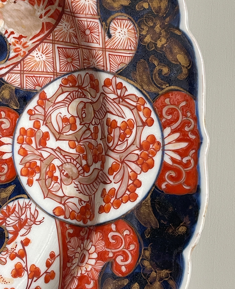 A large Oriental Imari scolloped edged plate with colourful hand painted depictions of Chrysanthemum flowers, fans, birds and cherry blossom. The underside sees a freeze of blue lilies - SHOP NOW - www.intovintage.co.uk