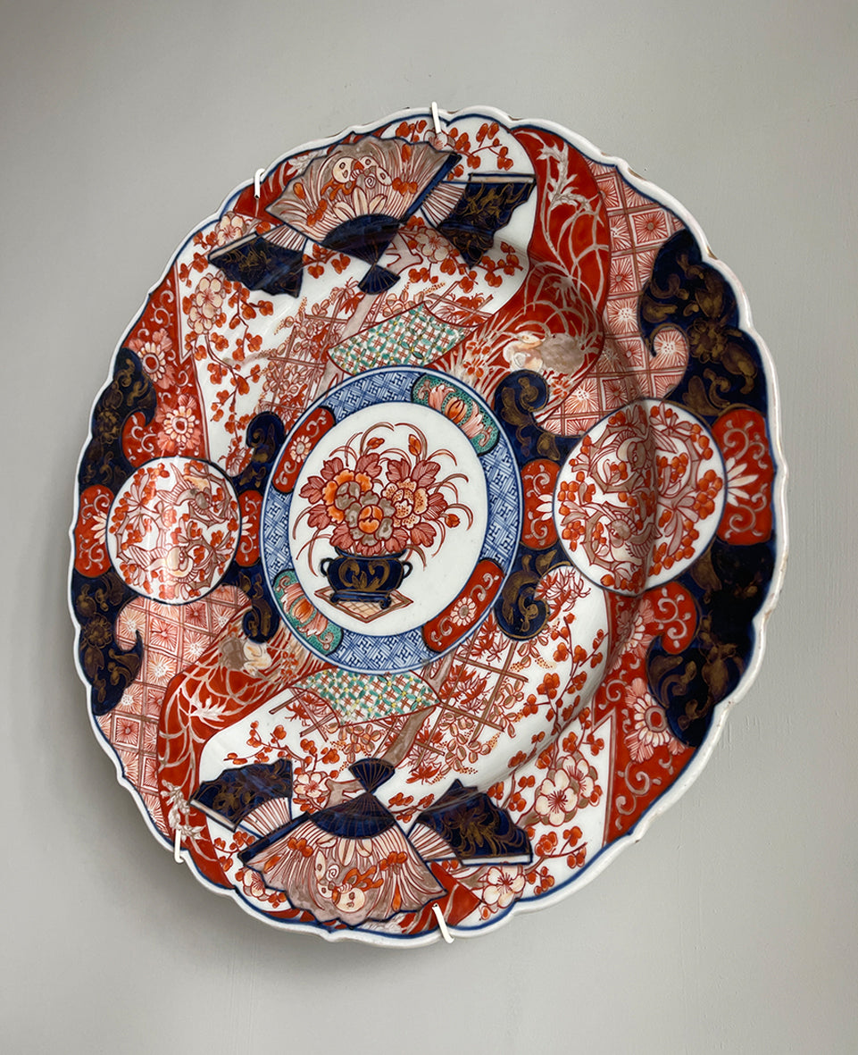 A large Oriental Imari scolloped edged plate with colourful hand painted depictions of Chrysanthemum flowers, fans, birds and cherry blossom. The underside sees a freeze of blue lilies - SHOP NOW - www.intovintage.co.uk