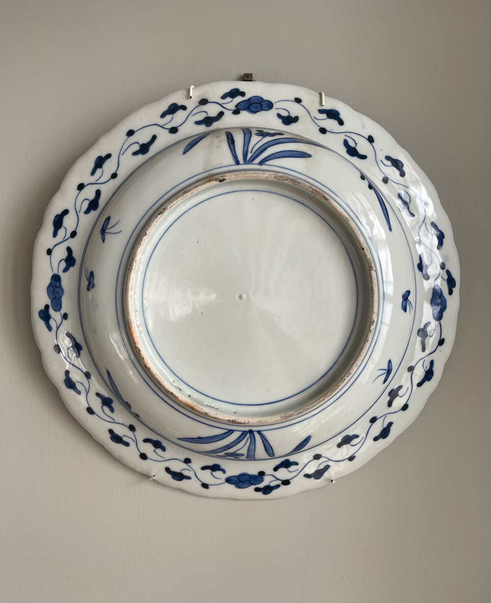 A large Oriental Imari scolloped edged plate with colourful hand painted depictions of Chrysanthemum flowers, fans, birds and cherry blossom. The underside sees a freeze of blue lilies - SHOP NOW - www.intovintage.co.uk