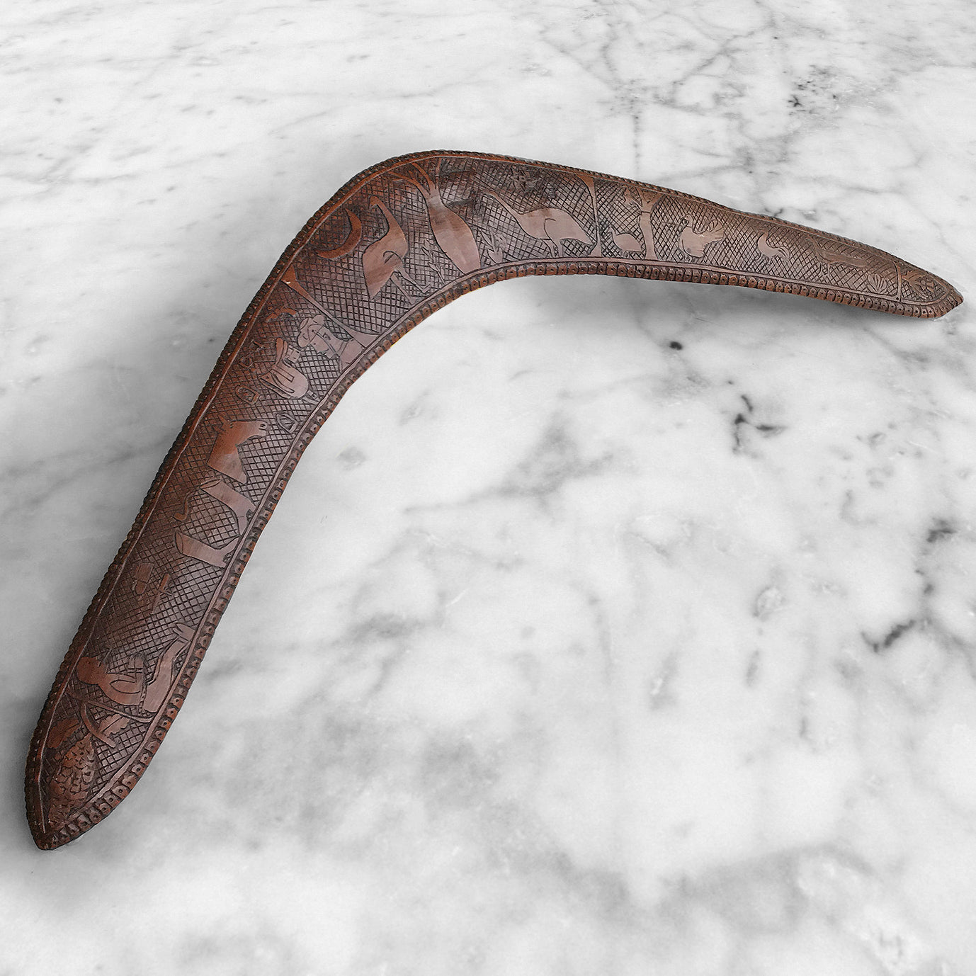 Wonderfully carved Antique Australian Boomerang with amazing naive carving and a beautiful warm colour. On the right side the carved elements include 2 emus, a cockerel, a turkey, a peacock a pea hen and a thistle, whilst on the left side we have a chap smoking a pipe, a knife, a cap, riding boots, pipe, horse, saddle, stirrups, hand cuffs, revolver, and Australian in an army hat. The background has a crosshatch design whilst the edge is finished in a carved dotted pattern - SHOP NOW - www.intovintage.co.uk